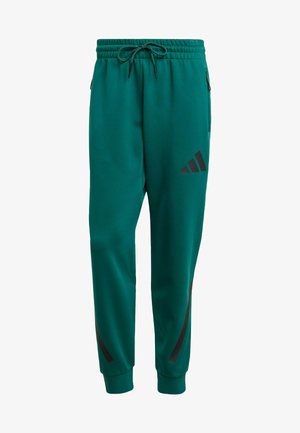 Zelené sportovní joggers vyrobené z texturované látky, vybavené elastickým pasem na šňůrku, zipovými kapsami a černými logovými akcenty.