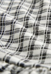 Tela de cuadros en blanco y negro con pliegues diagonales, mostrando un patrón suave y texturizado de líneas y cuadros que se cruzan.