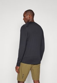 Langaarm, donkergrijze shirt met platte naden en logo-detail op de linker mouw, gecombineerd met olijfgroene shorts met een logo.