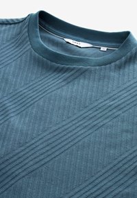 Blå tekstureret t-shirt med diagonale ribbede mønstre. Har en rund halsudskæring og blødt stof for en komfortabel pasform.