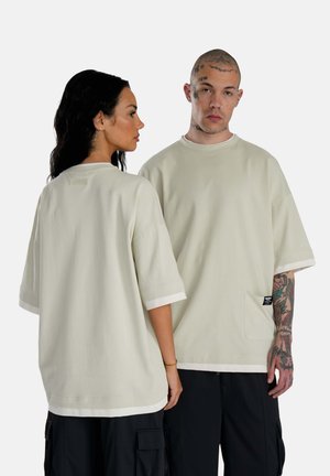 T-shirt a maniche corte dalla vestibilità rilassata in beige chiaro, con colletto rotondo, polsini bianchi a contrasto e taschino laterale con dettaglio etichetta.