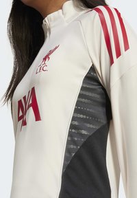 Vit Liverpool FC långärmad sporttröja med röda ränder på ärmarna, Liverpool-emblem och Axa-sponsorlogotyp på framsidan.