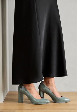 Groene laarzen van patenterleer met hoge hakken, een ronde neus en een chunky hak, gecombineerd met een zwarte rok. Gladde textuur, glanzende afwerking.