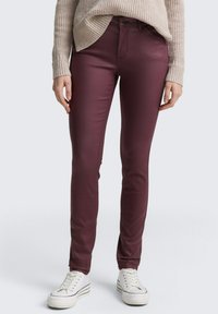 Pantalons slim-fit bordeaux en tissu extensible, avec une texture lisse, des poches à l'avant et associés à des baskets blanches.