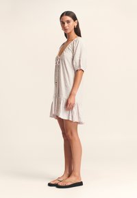 Gestreepte korte jurk met pofmouwen, een diepe halslijn en een gerimpelde zoom. Heeft een strikdetail aan de voorkant. Het materiaal lijkt lichtgewicht.
