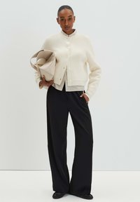 Cream cardigan with ribbed cuffs and collar, featuring buttons down the front, paired with black wide-leg trousers and a beige bag.