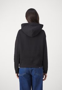 Black hooded sweatshirt with a relaxed fit, ribbed hem, and cuffs; worn with blue high-waisted jeans; smooth texture.