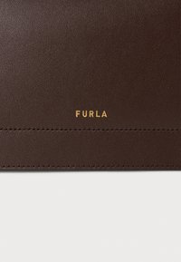 Hnedý kožený držiak na karty s hladkým povrchom, zlatým logom "FURLA" a viditeľným prešívaním pozdĺž okrajov. Kompaktný a štíhly dizajn.