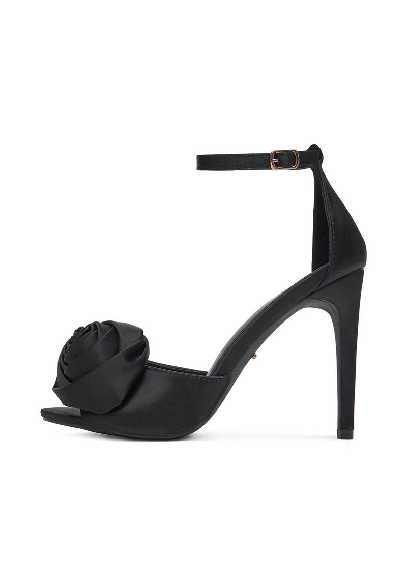 Czarne sandały na wysokim obcasie z zapięciem na kostkę i dużym detalem z tkaniny w kształcie róży z przodu, na otwartym palcu.