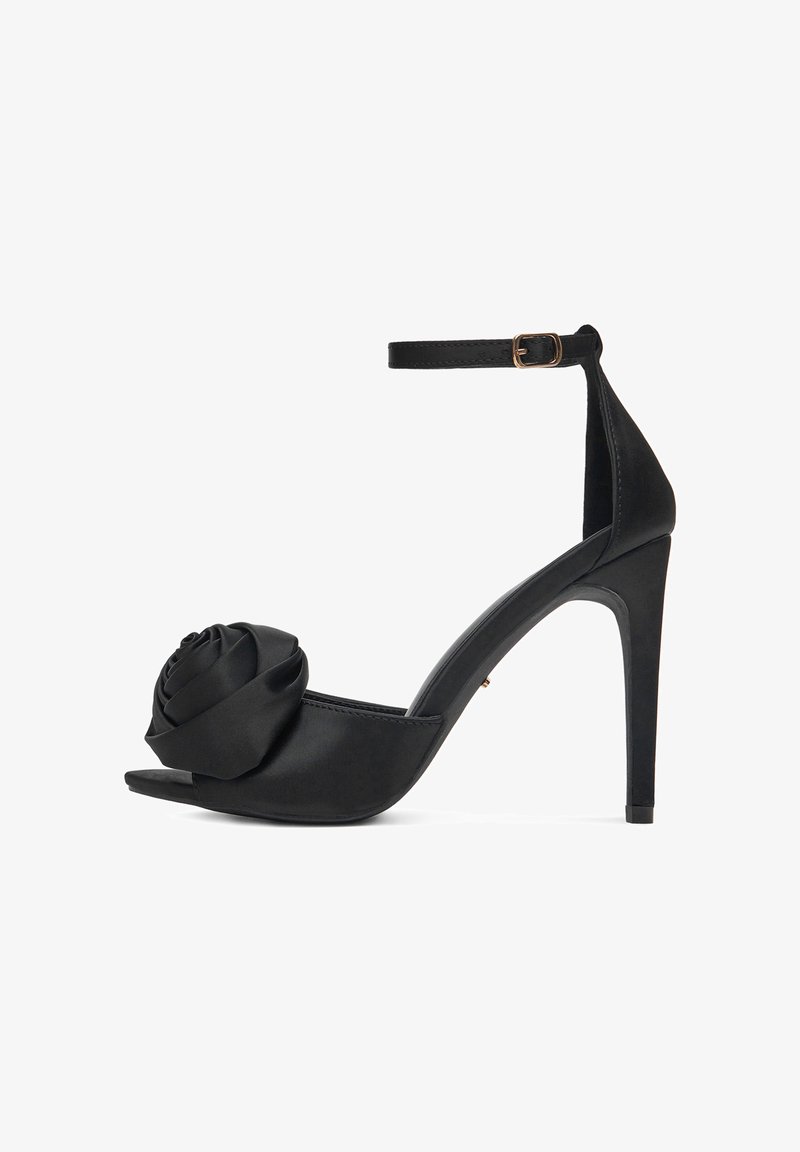 Czarne sandały na wysokim obcasie z zapięciem na kostkę i dużym detalem z tkaniny w kształcie róży z przodu, na otwartym palcu.