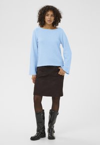Pull bleu clair et doux à manches longues ; jupe en daim marron longueur genou avec poches ; bottes noires brillantes montant jusqu'aux genoux avec boucles.