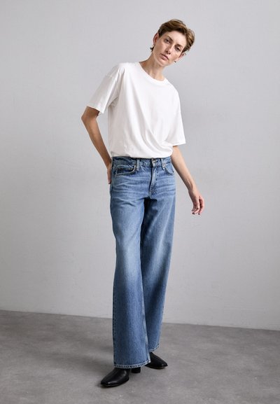 Wide-leg light blue jeans paired with a plain white t-shirt. The jeans feature a classic five-pocket design and slight fading. Black shoes accent the outfit.