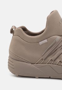 Wasserfeste taupe Sneaker mit einer glatten Oberfläche, hohen Kragen, elastischen Seitenakzenten und einer robusten Gummisohle für besseren Grip.