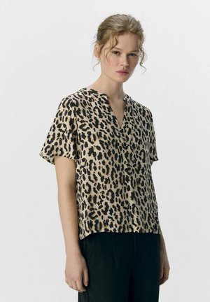 Blouse à manches courtes imprimée léopard en beige et noir, avec un décolleté en V et un tissu doux, associée à un pantalon noir ample.
