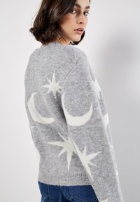 Grauer Strickpullover mit weißen Mustern von Halbmond und Sternen, abgerundetem Halsausschnitt und geripptem Saum. Weicher Stoff, normale Passform.