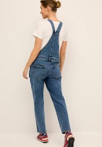 Denim kombinesid reguleeritavate rihmadega, lõdva istuvusega, helesinine värv, kaks tagataskut, koos valge t-särgi ja punaste tossudega.