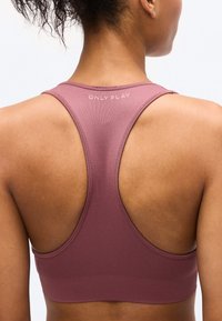 Η πλάτη γυναίκας που φοράει αθλητικό σουτιέν με ράντες racerback σε μωβ απόχρωση, με το κείμενο «ONLY PLAY» κοντά στη λαιμόκοψη.