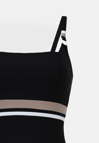 Sort bikinitop med justerbare stropper, der har et design med horisontale farveblok-accents i beige, hvid og sort. Glat tekstur.