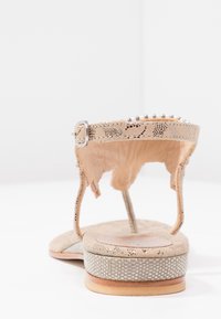 Beżowe płaskie sandały z plecioną teksturowaną podeszwą, z paskiem na kostkę z srebrną klamrą i małymi dekoracyjnymi ćwiekami wzdłuż górnej krawędzi.