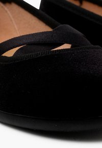 Ballerine in suede nero con punta arrotondata e fasce elastiche incrociate; interno liscio con suola nera flessibile.