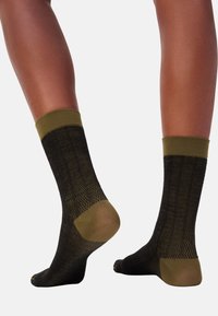 Schwarze und olivgrüne gemusterte Socken mit einem gerippten Design, ausgestattet mit kontrastierenden Bündchen und Ferse. Weicher Stoff, mittlere Höhe, enganliegende Form.