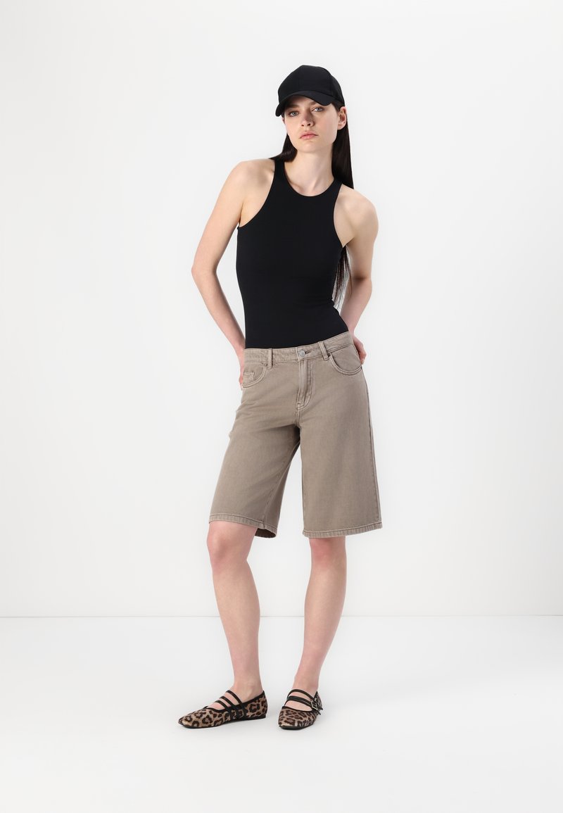 Un body sans manches noir, un short beige arrivant au genou et des chaussures plates à imprimé léopard. L'ensemble présente un design minimaliste et une silhouette ajustée.