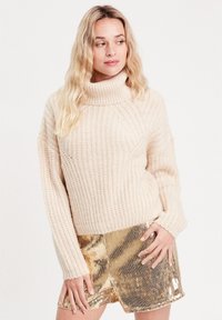 Pull en maille côtelée couleur crème à col roulé, associé à une mini-jupe en sequins dorés brillants.