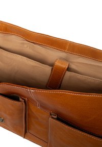 Interno di una borsa in pelle color cuoio con una texture morbida, caratterizzato da un compartimento principale, una sezione imbottita e dettagli cuciti.