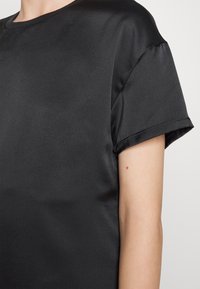 Schwarzes Satin-T-Shirt mit rundem Ausschnitt und kurzen, gerollten Ärmeln, das eine glatte Textur und eine lockere Passform aufweist.