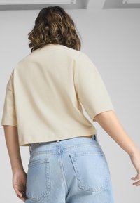 Kortærmet, lys beige crop top med en afslappet pasform, parret med højtaljede lys blå denimjeans med baglommer og diskret syninger.