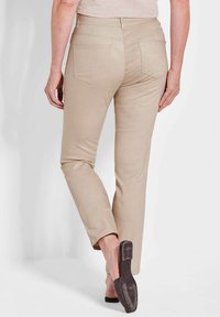 Pantaloni beige con una texture liscia, gamba affusolata e due tasche posteriori. Abbinati a una scarpa bassa semplice.