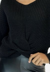 Il pullover nero lavorato a maglia presenta un design twistato in vita, un tessuto testurizzato e una vestibilità comoda, abbinato a leggings neri.