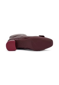Botín de cuero burdeos con tacón bloque, suela texturizada y punta redondeada. Cuenta con una pestaña lateral para facilitar su uso.