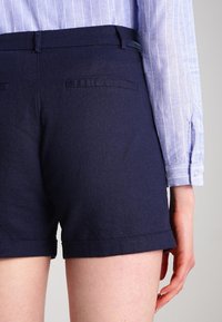 Mörkblå shorts i vävt tyg, med rak passform, uppvikta fållar och två bakfickor med en subtil textur.