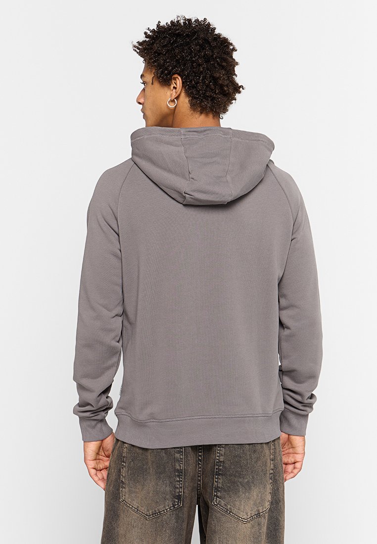 Felpa grigia con finitura texturizzata e cappuccio. Presenta polsini e orlo a coste. Indossata con pantaloni scuri e strappati.