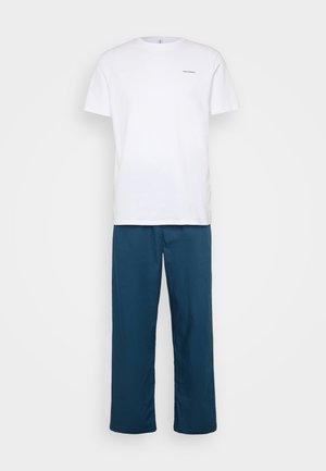 Bela bombažna majica s kratkimi rokavi in okroglim izrezom; v kombinaciji z ohlapnimi teal hlačami, izdelanimi iz lahke tkanine.