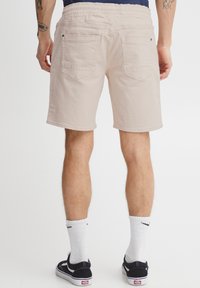 Pantaloni scurți bej deschis cu talie elastică, două buzunare în spate și croială dreaptă. Materialul pare moale, cu o textură fină.