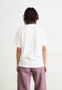 T-shirt en coton blanc à manches courtes et col rond, vue de dos, associée à un pantalon cargo rose avec poches latérales.