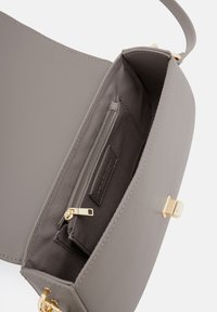 Grau Lederhandtasche mit einer glatten Außenseite. Das Innere bietet eine Reißverschlusstasche und einen einfachen metallenen Verschluss. Goldene Hardware-Akzente.