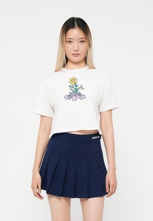 T-shirt bianco corto con grafica di un fiore e un nastro. Abbinato a una gonna plissettata blu navy con cintura elastica e dettaglio del logo.