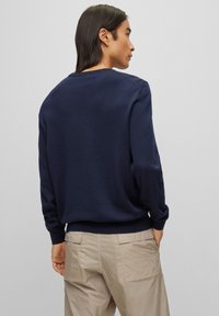 Σκούρο μπλε, μακρυμάνικη μπλούζα με κλασικό στρογγυλό λαιμό. Λείο υλικό, ριμπέ μανσέτες και τελείωμα. Φοριέται με ανοιχτό μπεζ, υφασμάτινα παντελόνια.