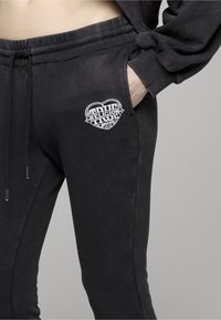 Czarne spodnie dresowe z miękkiego materiału, z haftowanym białym logo serca na górnej lewej kieszeni oraz elastycznym paskiem w talii.
