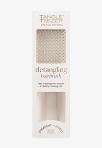 Brosse à cheveux démêlante dans un étui blanc, avec une surface texturée, un manche lisse et une fenêtre transparente affichant la brosse.