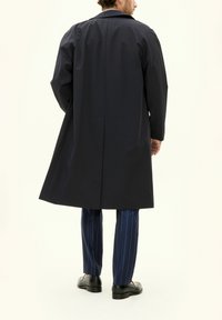 Marineblauer wasserdichter Trenchcoat mit geradem Schnitt, breiten Revers und langen Ärmeln. Kombiniert mit marineblauen gestreiften Hosen und schwarzen Schuhen.