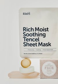 Klairs Rich Moist Soothing Tencel Sheet Mask-pakningen har fet svart tekst på hvit bakgrunn. En rosa såpebar og sirkulære aksenter under.