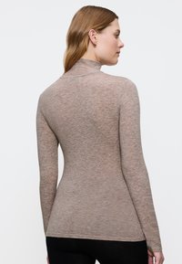 Getailleerde lange mouwen turtleneck in lichtbruin, vervaardigd van zachte, transparante breistof. Heeft een hoge kraag en een naadloos ontwerp.