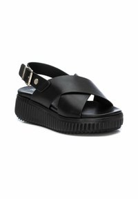 Sandalias de cuña negras hechas de cuero suave con un diseño de tiras cruzadas, correa para el tobillo ajustable y suela de goma texturizada.