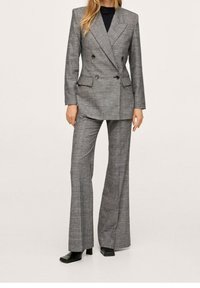 Szara dwurzędowa marynarka w kratę z klapami z wycięciami, zestawiona z dopasowanymi rozkloszowanymi spodniami. Materiał: tkanina tkana. Akcenty: czarne guziki.