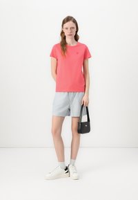 Rosa t-skjorte med korte ermer og rund hals, lyseblå shorts, hvite joggesko og en liten svart veske. Enkelt, uformelt antrekk.