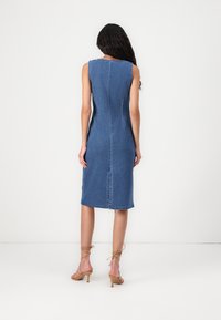 Džinsinis midi suknelė su prigludusia siluetu, be rankovių dizainu ir nugaros skeltuku. Pasižymi matomais siūlais ir vienspalve mėlyna spalva.